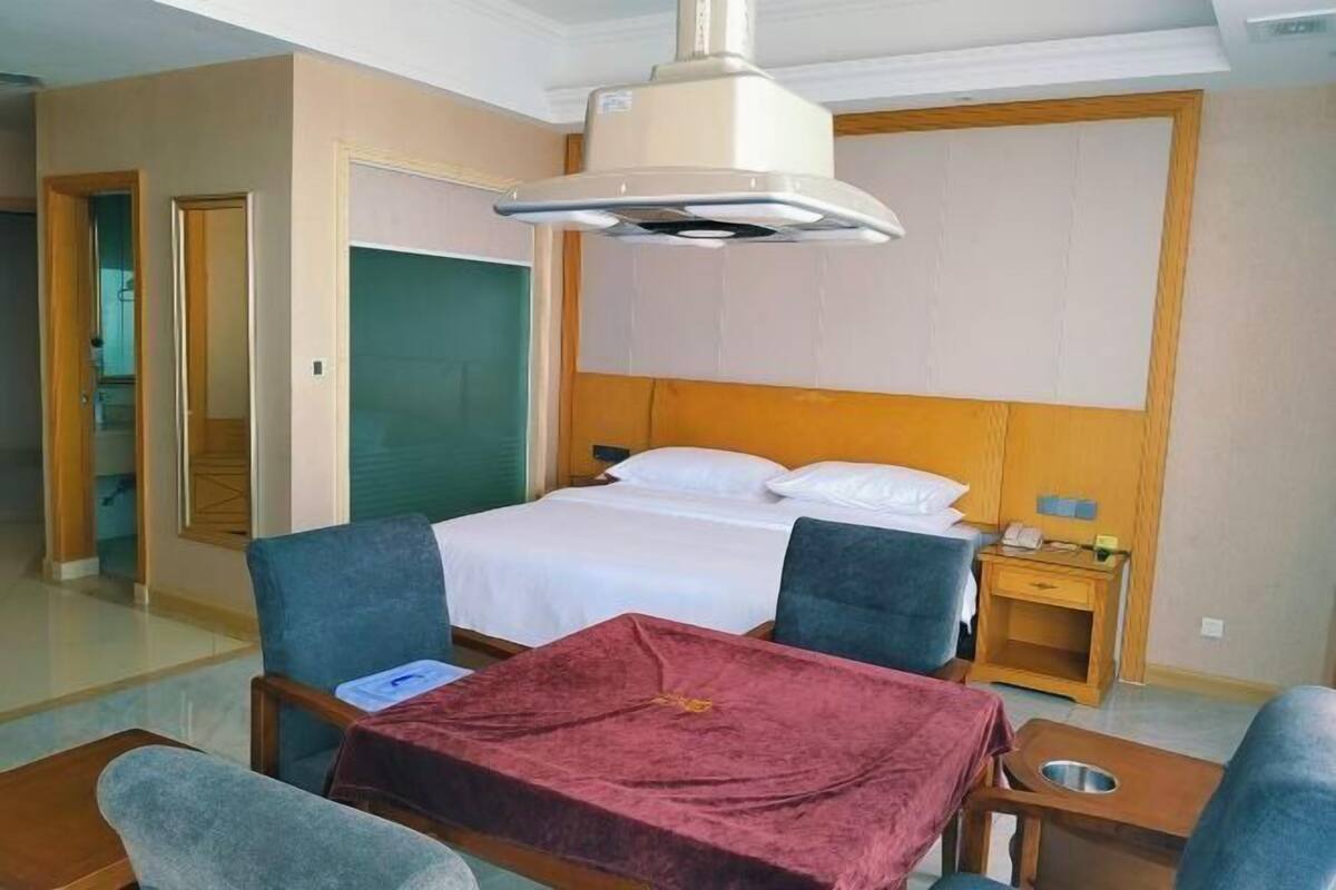 A hotel room with a bed, two chairs, a small table, a bedside table, and a ceiling light.