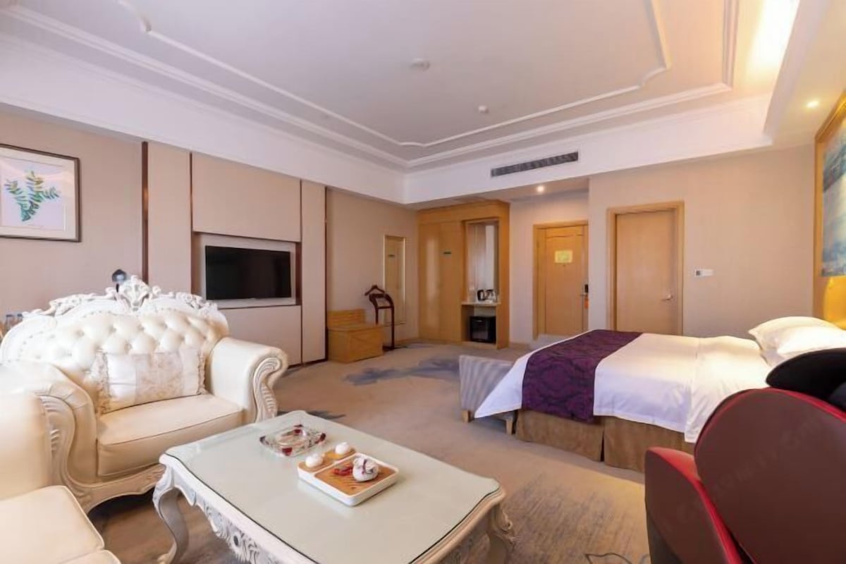 A hotel room with a large bed, a sofa, a television, and a dining table with a tray of food.