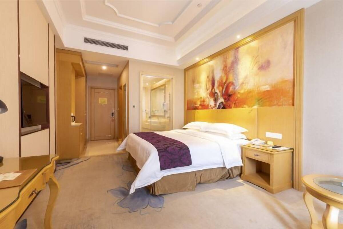 A hotel room with a bed, bedside table, and a large abstract painting on the wall.