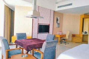 A hotel room with a bed, a desk with a chair, a TV, and a table with chairs.