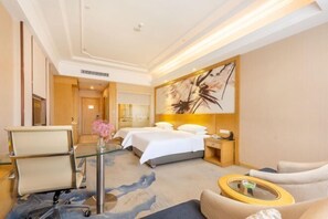 A hotel room with a bed, a desk, a chair, and a sofa.