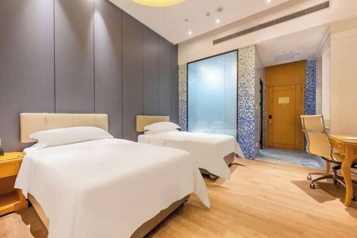 A hotel room with two beds, a desk, a chair, and a large window.