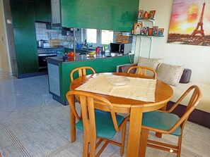 Kompakti keittiö, jossa on ruokailutila, vihreä työtaso ja sohva, jossa on koristetyyny.