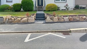 Una casa a due piani con un ingresso principale, un piccolo giardino e un vialetto lastricato.