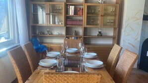 Un'area pranzo con un tavolo in legno e sedie in vimini, affiancata da librerie a vetro piene di libri e oggetti decorativi.