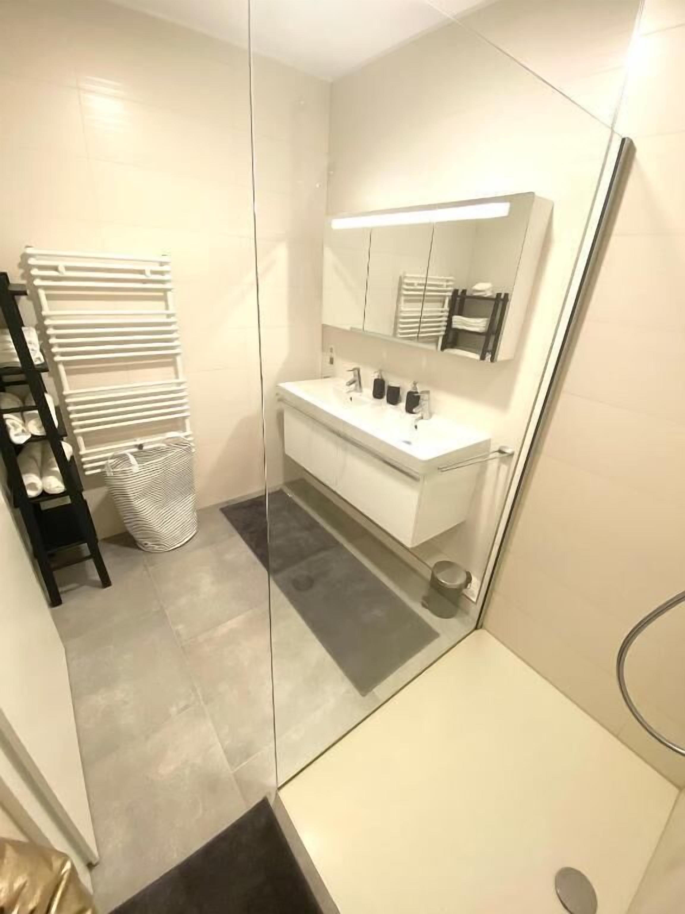 A modern bathroom with a glass shower enclosure, a white vanity with a mirror, and a towel rack.