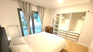 Ein Schlafzimmer mit Bett, Kleiderschrank, Schreibtisch und Blick ins Freie.