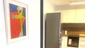 Ein modernes Wohnzimmer mit einem grauen Sofa, einem gerahmten abstrakten Gemälde und einer Küche im Hintergrund.