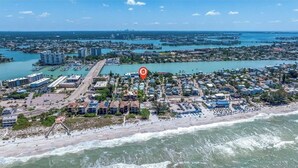 An aerial view of a coastal town with a marina, beachfront properties, and a prominent hotel with a red marker. - "Seaside Serenity: Stunning Beach House Retreat" (Treasure Island)