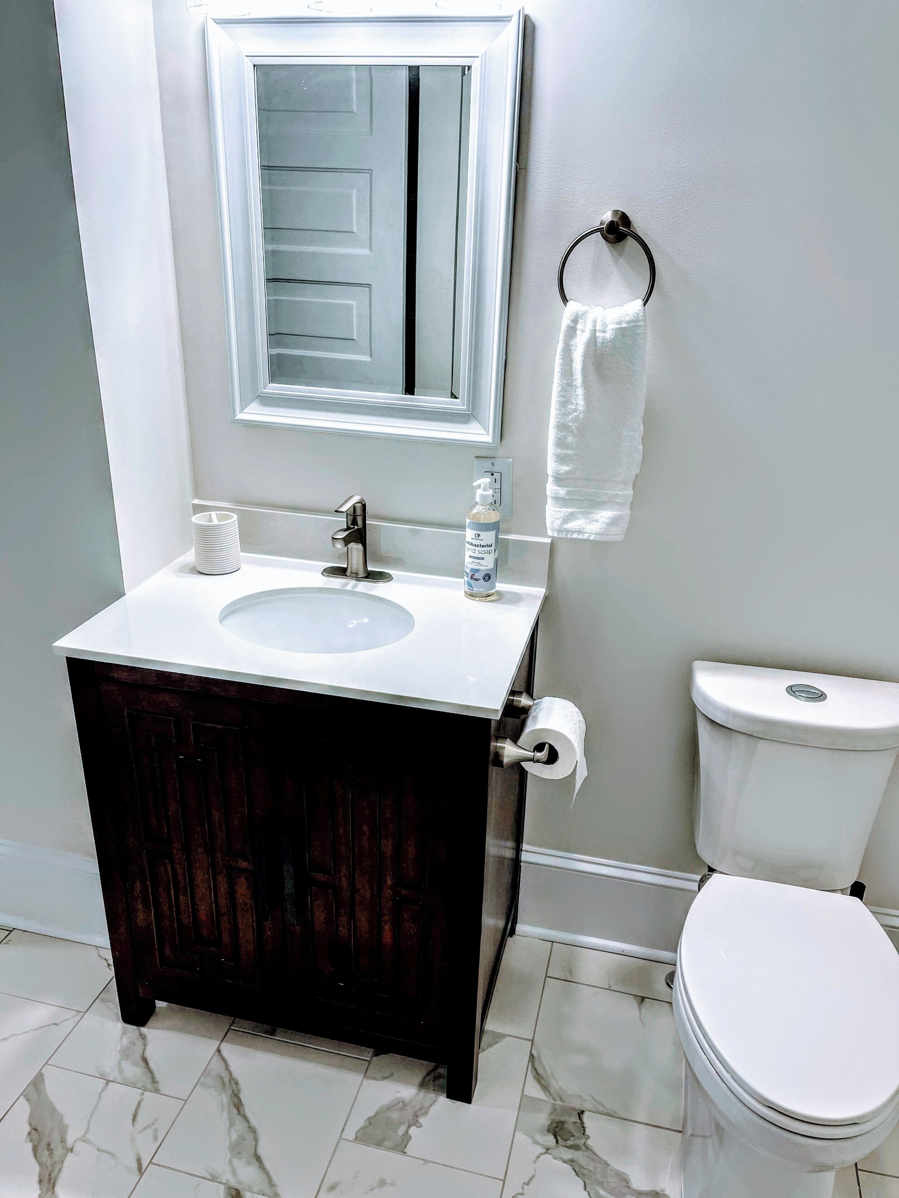 A bathroom with a white sink, dark wooden vanity, a mirror above the sink, a toilet, and a towel hanging on the wall.