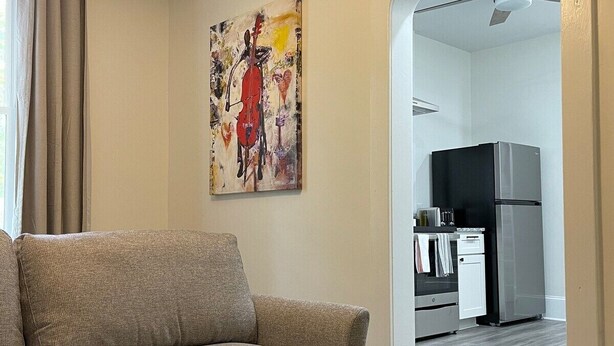 En stue med sofa, et billede og et køkken, der kan ses gennem en åben dør.
