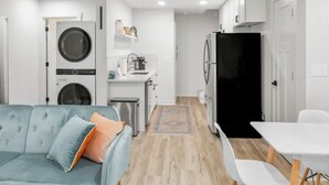 Un espace de vie compact comprenant un canapé, un petit coin cuisine, un lave-linge et un réfrigérateur.