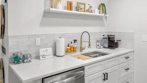 Une cuisine moderne avec des meubles blancs, un lave-vaisselle en acier inoxydable, un évier avec un robinet doré et une machine à café.