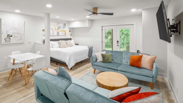Une chambre à coucher moderne avec un lit, un canapé bleu, une table basse ronde en bois et un bureau blanc avec des chaises.
