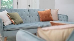 Un canapé bleu clair agrémenté de plusieurs coussins de différentes couleurs, placé dans une pièce aux murs blancs, avec une porte visible au fond.