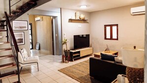 A modern living room with a staircase, a flat-screen TV, a wooden entertainment unit, and a large window. - Oasis en Centro Histórico Alberca Playa 3 mins (Mazatlán)