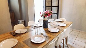 A dining table set for four with white plates, cutlery, and a vase of pink flowers. - Oasis en Centro Histórico Alberca Playa 3 mins (Mazatlán)