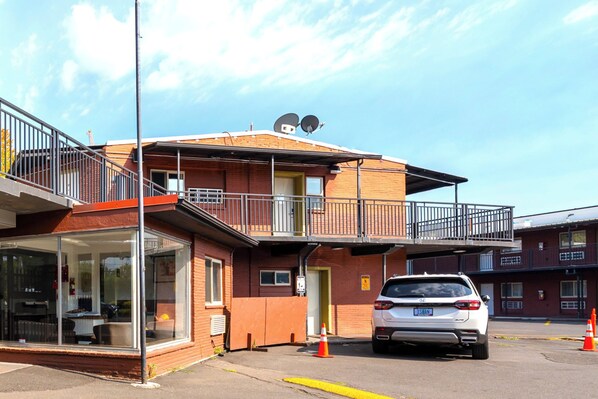 A two-story building with a balcony, a car parked in front, and a glass entrance.