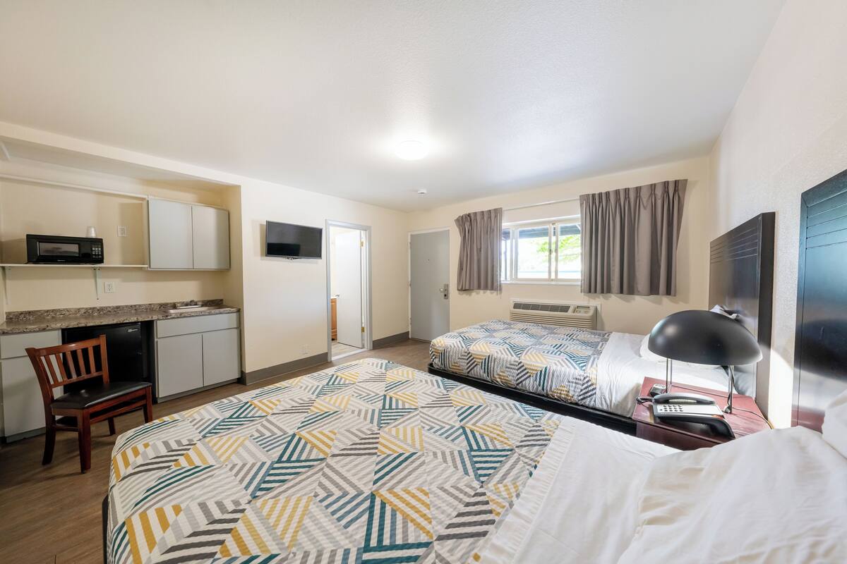 A hotel room with two beds, a desk with a chair, a microwave, a TV, and a window with curtains.