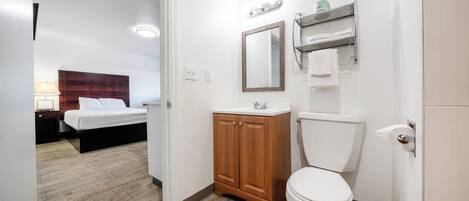 A hotel bathroom with a wooden cabinet, a toilet, a mirror, and a sink.