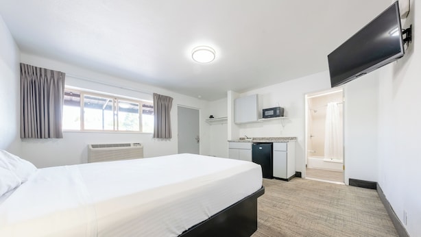 Hotellihuone, jossa on sänky, taulutelevisio, pieni keittiö ja kylpyhuone.