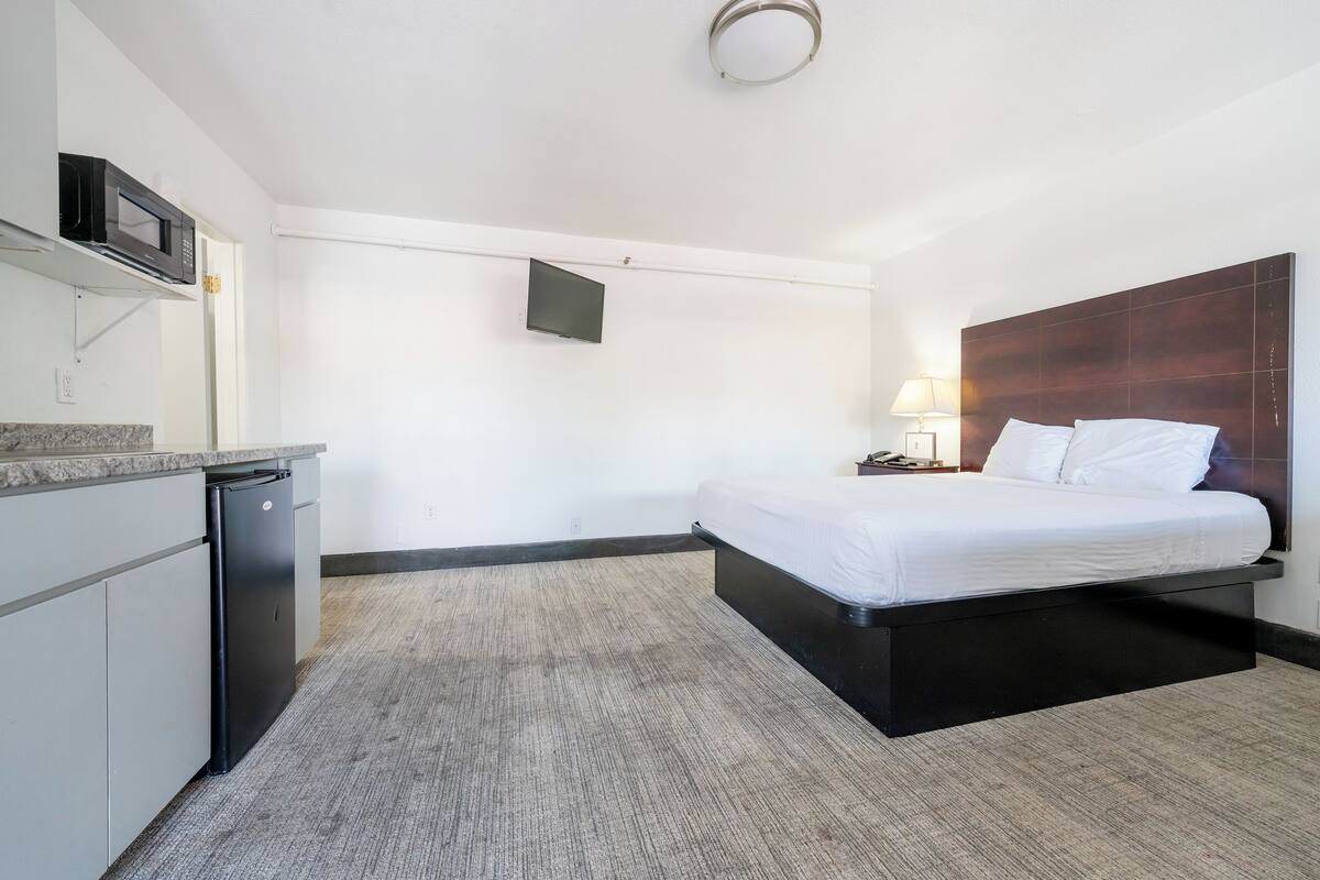 A hotel room with a bed, a desk with a microwave, a TV, and a lamp.