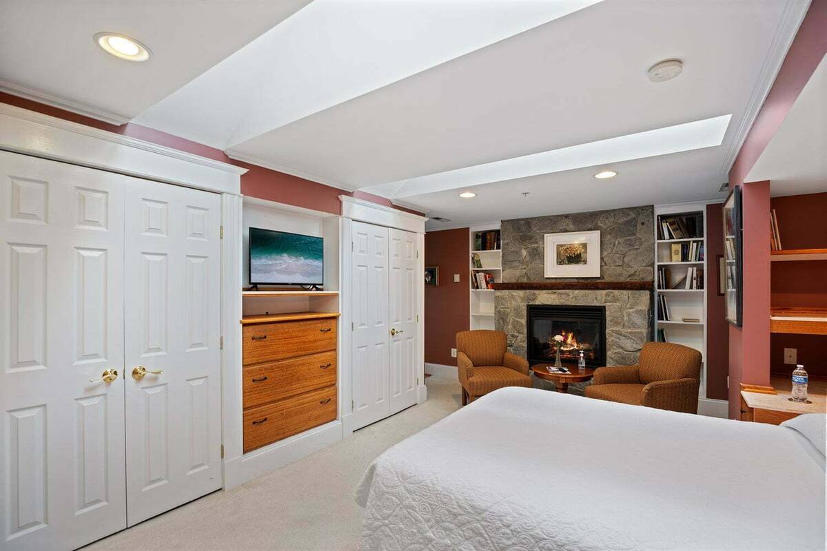 A bedroom with a large bed, a fireplace, a TV, and a bookshelf.