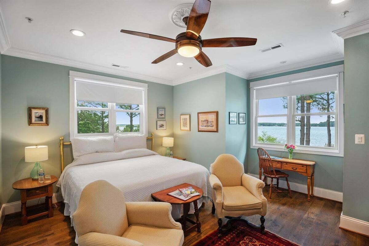 A bedroom with a large bed, two chairs, a desk, and a view of a lake.