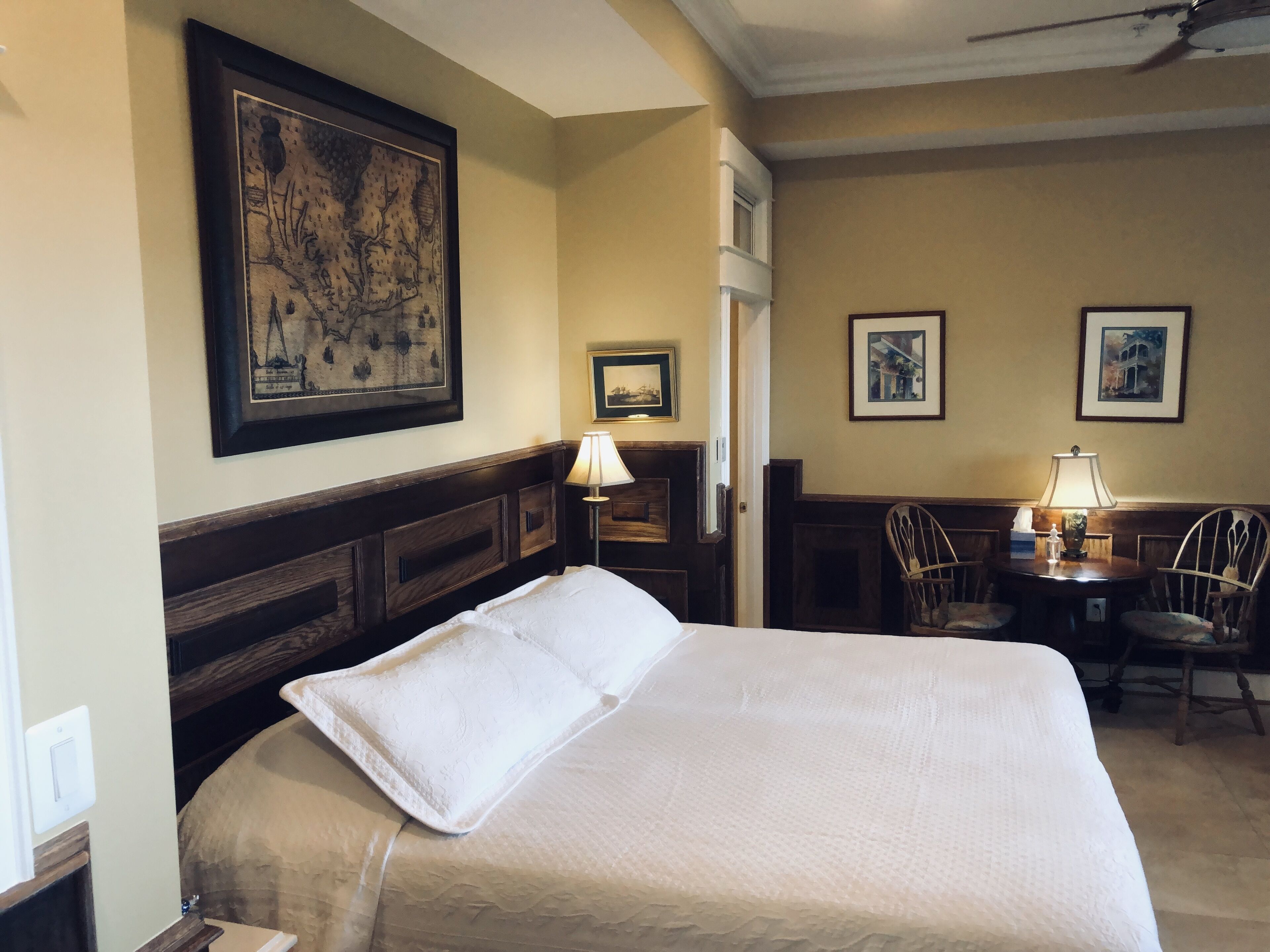 Una habitación de hotel con una cama grande, un escritorio con dos sillas y obras de arte enmarcadas en las paredes.