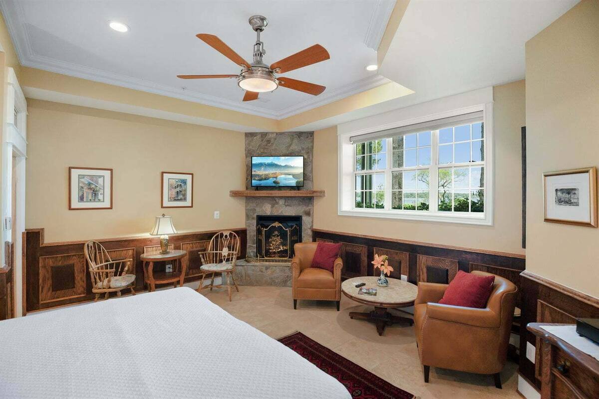A hotel room with a large bed, a fireplace, a stone wall, a television, and a window with a view.
