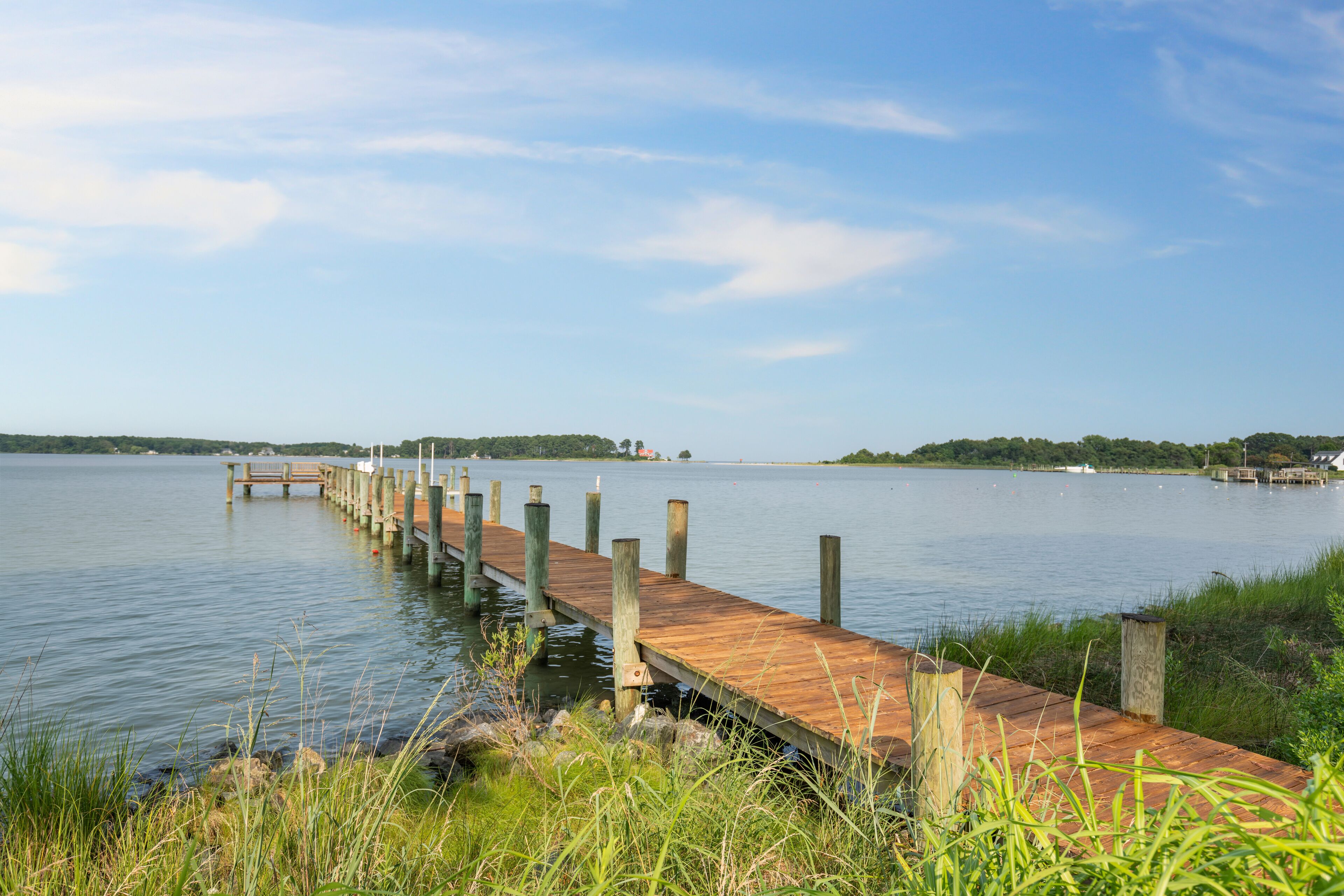 Een houten steiger die zich uitstrekt over kalm water, omringd door grasvelden en veraf gelegen land.