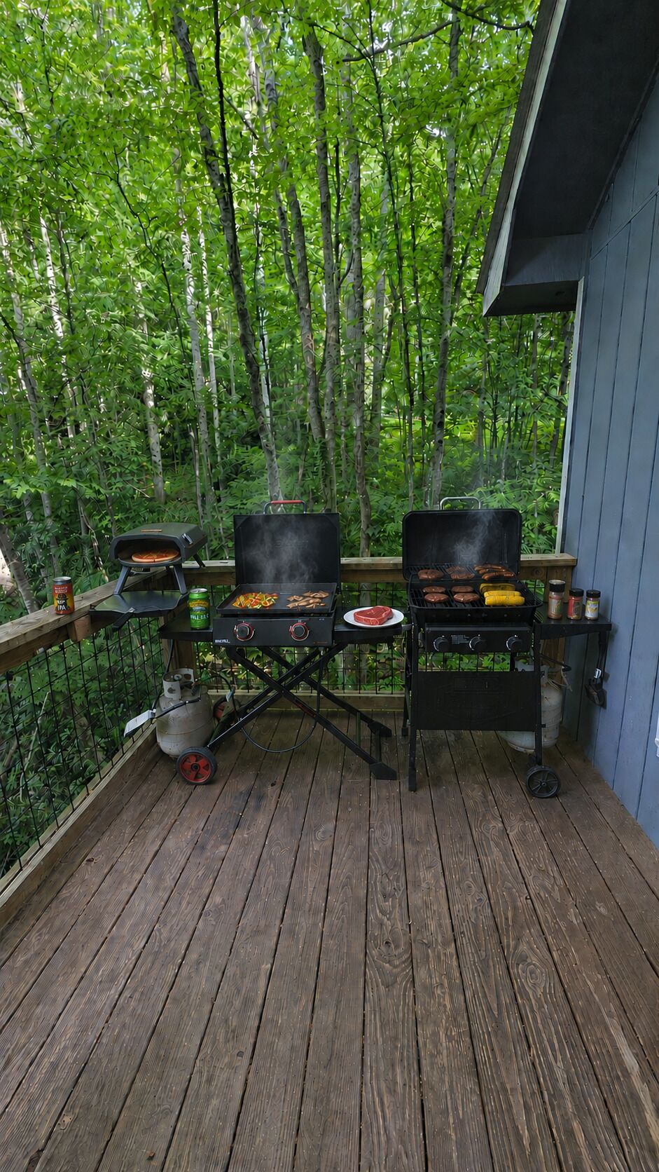 Una terraza de madera con dos parrillas para barbacoa, un bidón de gas y una pequeña mesa.