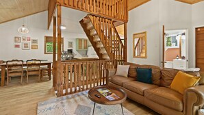 Un salón amplio con una escalera de madera, un sofá de cuero y una zona de comedor con muebles de madera.