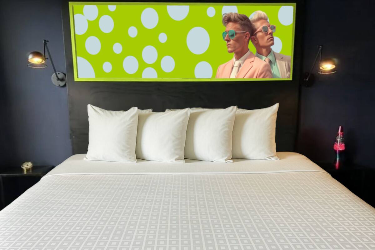 Een bed met een beddekleed met patroon, een hoofdbord met een groene en witte stippen wanddecoratie, en twee wandlampen.