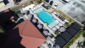Luchtbeeld van een dakzwembad met meerdere ligbedden en parasols, omringd door gebouwen.