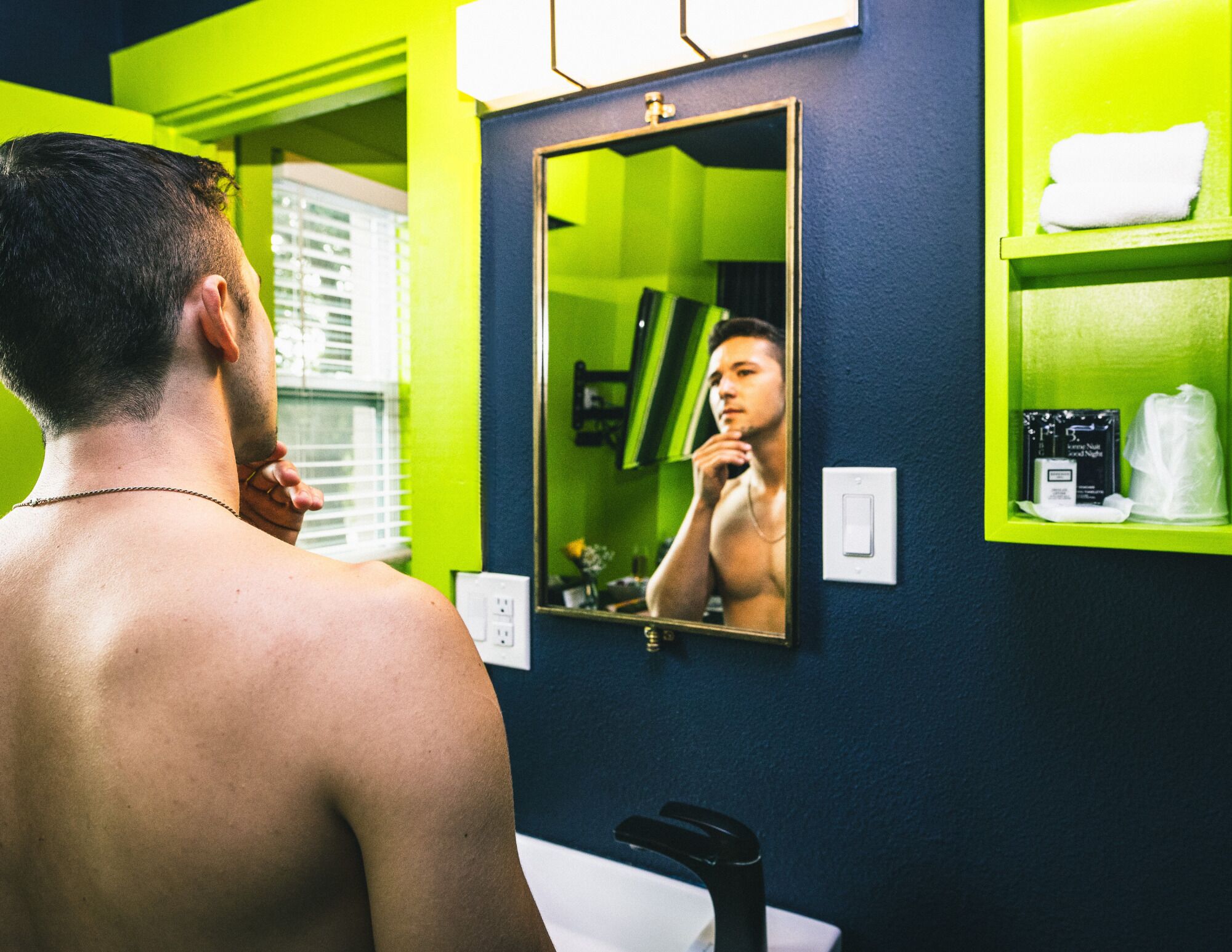 A man in a bathroom with a mirror, green walls, and a sink.