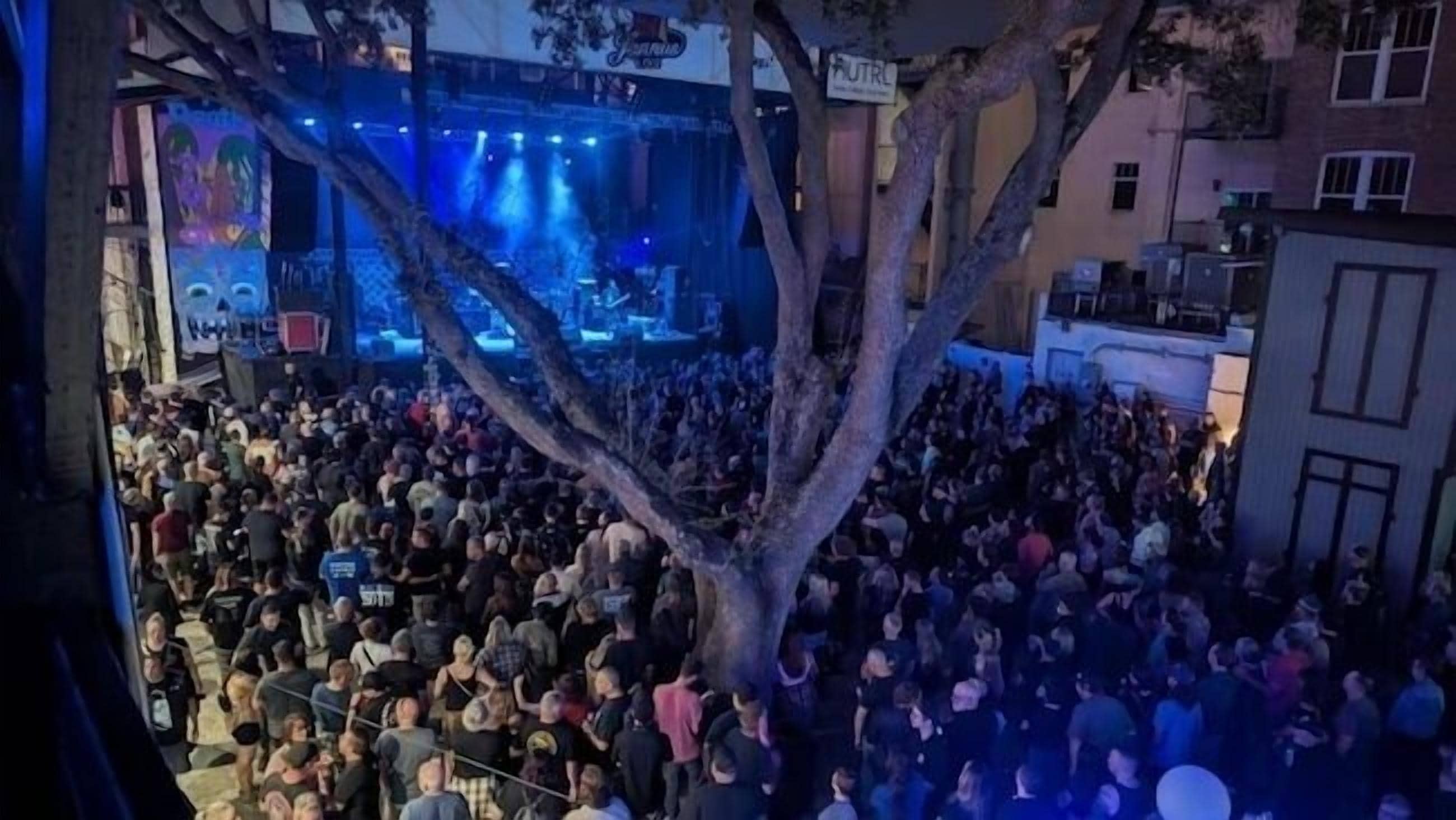 Un evento al aire libre concurrido, con un escenario y árboles al fondo.