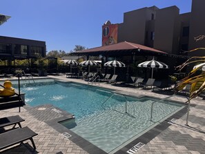 A swimming pool with lounge chairs and umbrellas, surrounded by buildings.