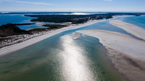 Luchtbeeld van een kustgebied met een strand, waterlichamen en een brug in de verte.
