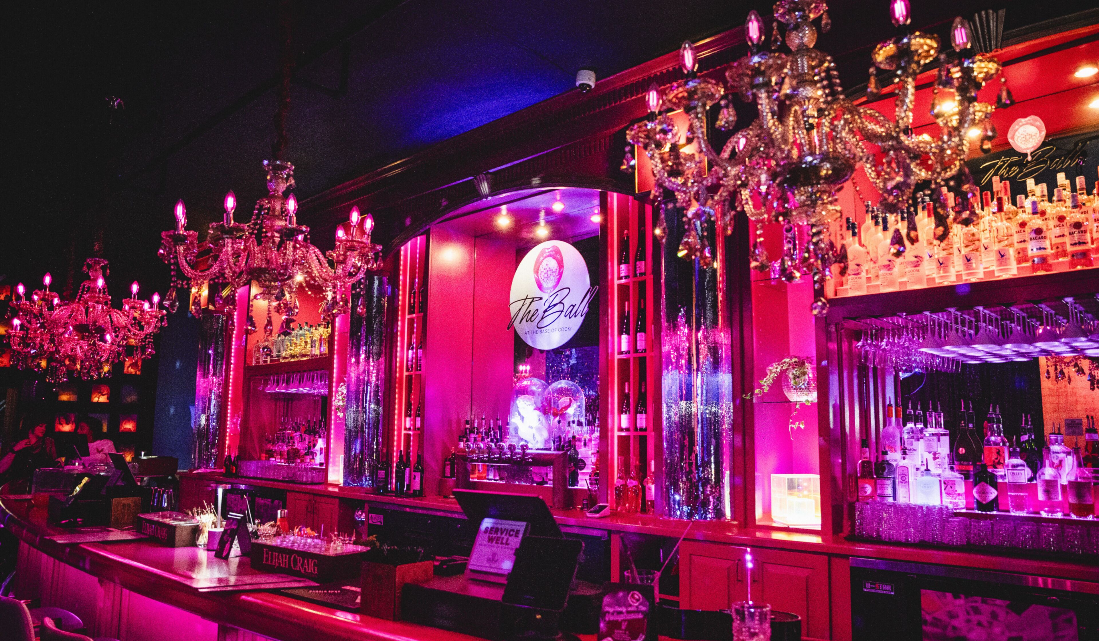 Un bar avec un néon, des lustres et des étagères remplies de bouteilles d’alcool.