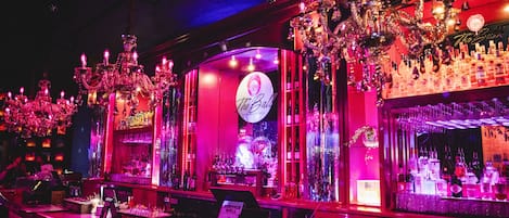 A bar with a neon sign, chandeliers, and shelves of liquor bottles.