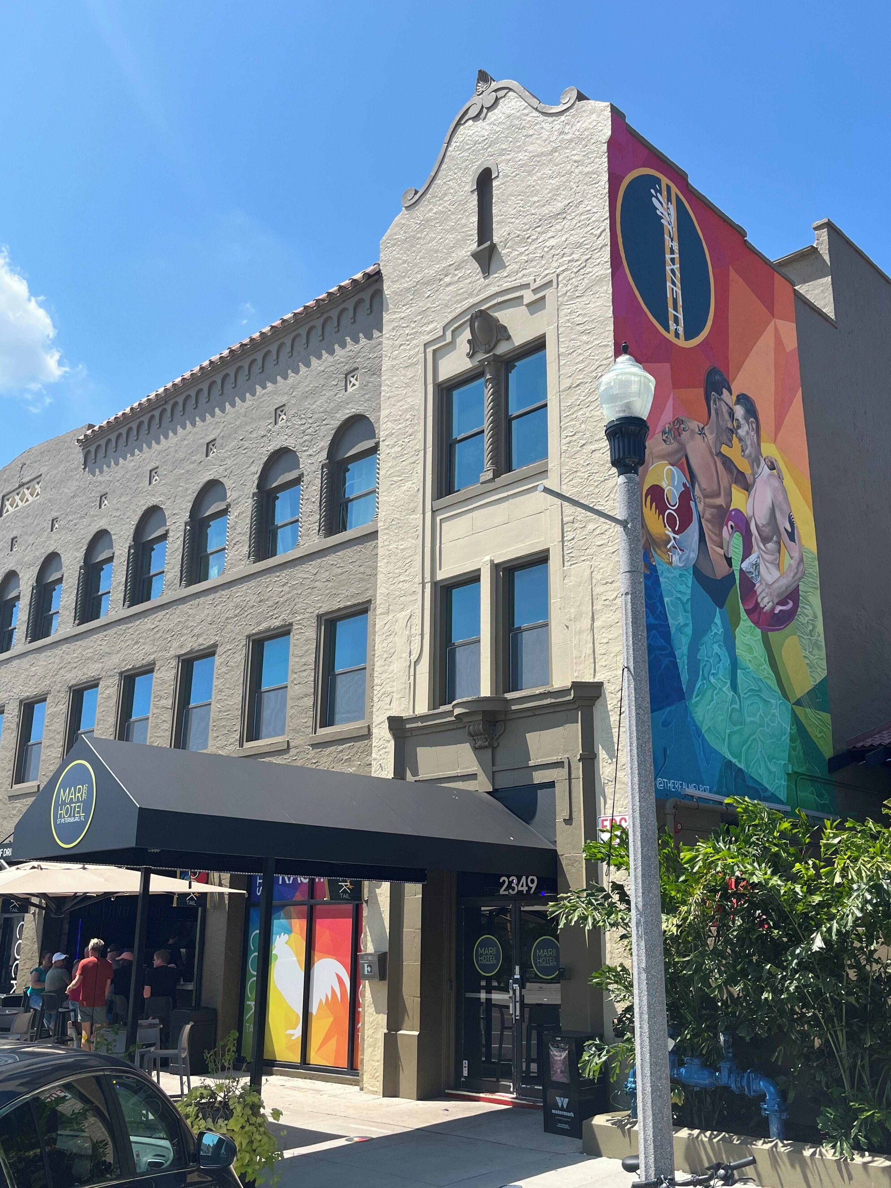 A hotel with a large mural on the side, a covered outdoor seating area, and a clear blue sky.