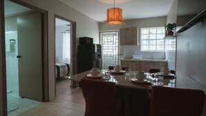 Eine moderne Küche mit Essbereich, ausgestattet mit einem für vier Personen gedeckten Tisch, weißen Tellern und Tassen, einer Hängelampe und Blick ins angrenzende Badezimmer.