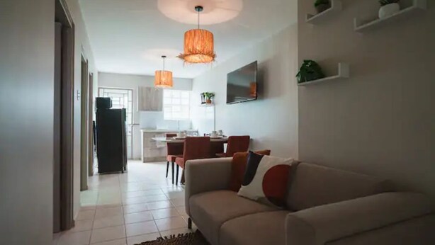 Ein modernes Wohnzimmer mit einer Couch, einem Essbereich mit Stühlen und einer Küche im Hintergrund.