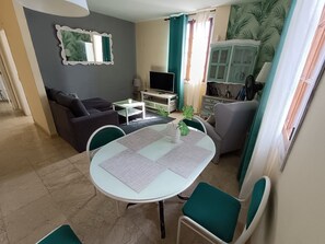 Una sala de estar con un sofá, un televisor, una mesa de comedor con sillas y un aparador con adornos.