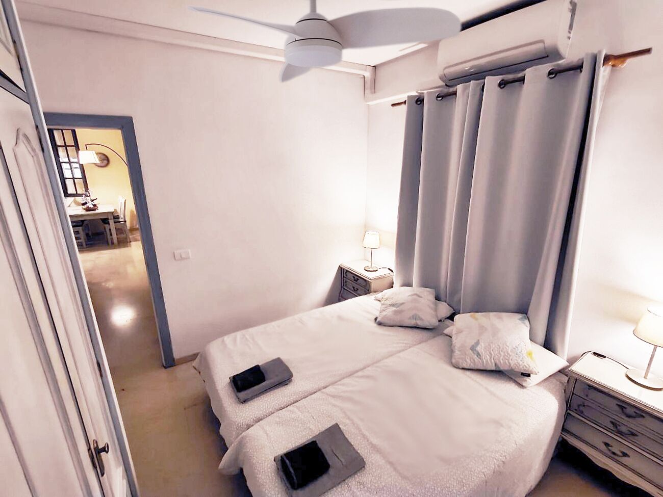 Una camera da letto con un letto, comodini, una ventola a soffitto e vista su un corridoio.
