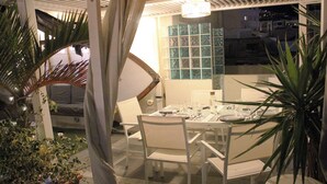 An outdoor dining area with a white table and chairs, surrounded by potted plants and a view of the city at night. - Atlantic Terrace. An oasis in the city. (Santa Cruz de Tenerife)