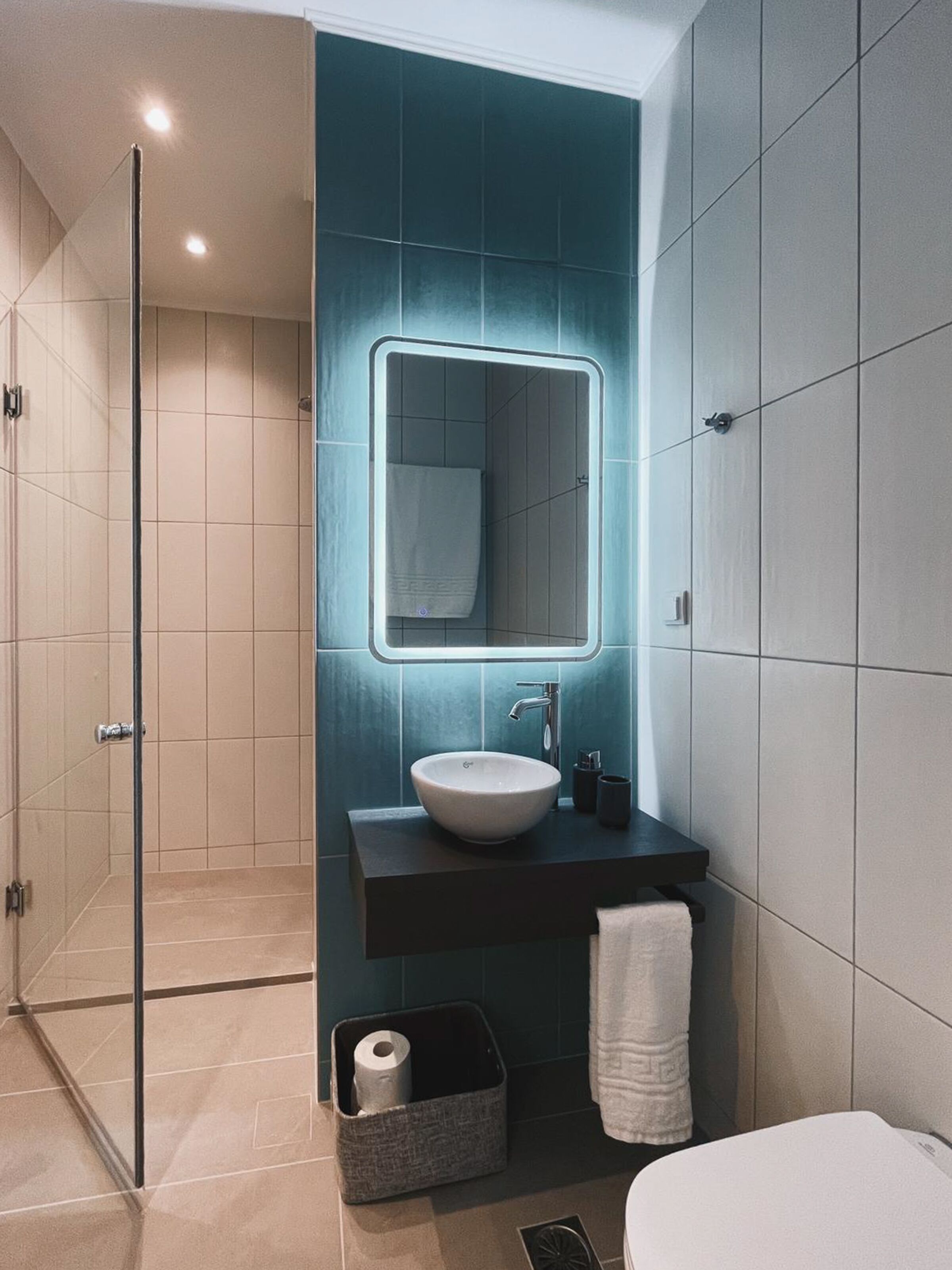 A modern bathroom with a glass shower enclosure, a large mirror, a white sink, and a dark countertop.