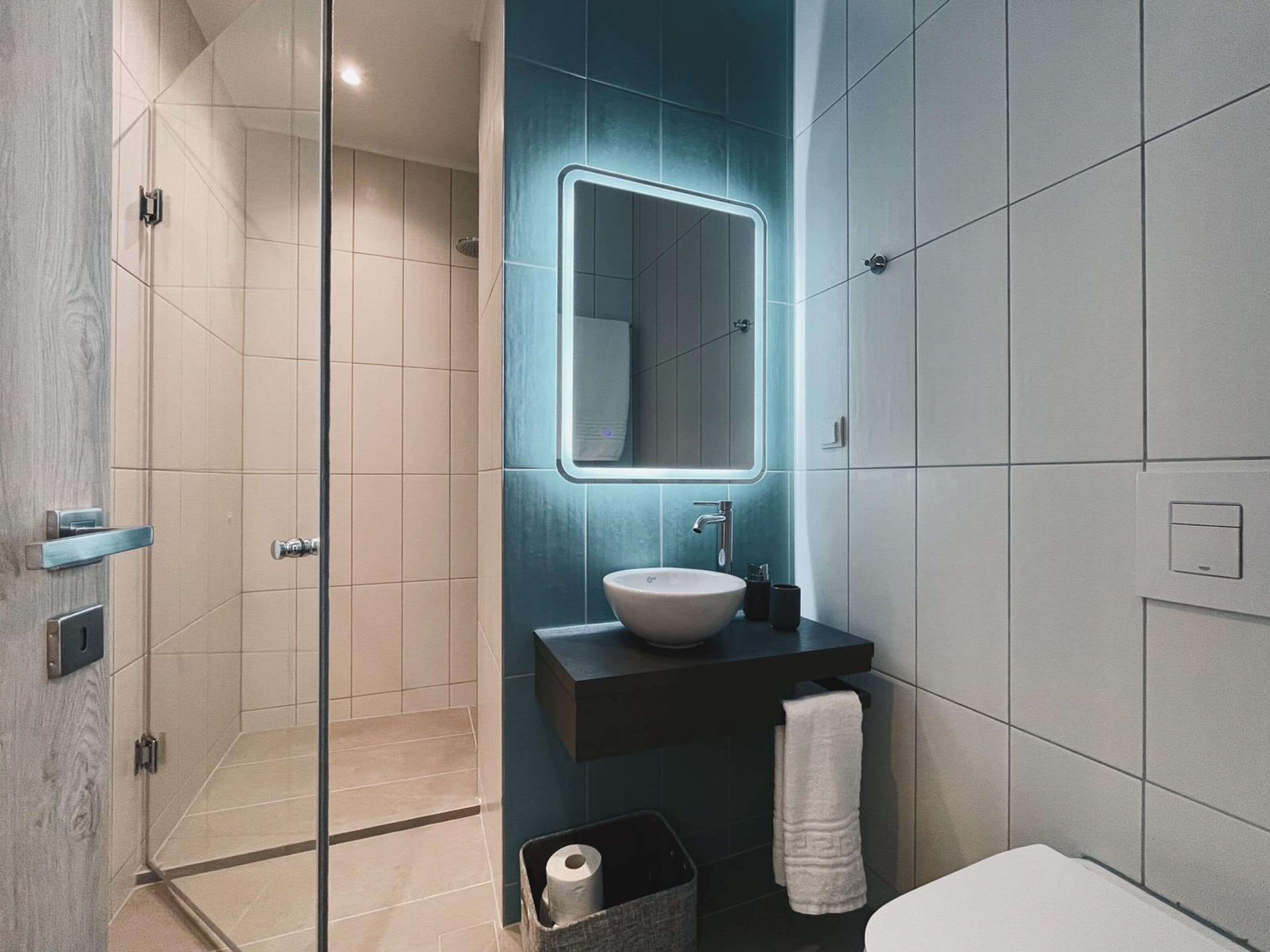 A modern bathroom with a glass shower enclosure, a large mirror, a sink with a dark countertop, and a white toilet.