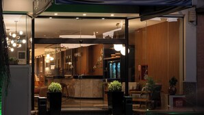 Ingresso di un hotel con area esterna coperta, reception e interni con posti a sedere e piante.